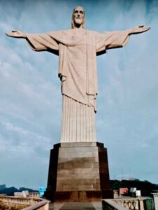 Imagem impressionante do Cristo Redentor, majestosamente situado no topo do morro do Corcovado, no Rio de Janeiro. A estátua icônica com os braços abertos em um gesto de acolhimento e paz, contrastando com o céu azul e a paisagem exuberante ao redor. Uma representação imponente da cultura e da fé brasileira.