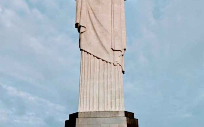 Imagem impressionante do Cristo Redentor, majestosamente situado no topo do morro do Corcovado, no Rio de Janeiro. A estátua icônica com os braços abertos em um gesto de acolhimento e paz, contrastando com o céu azul e a paisagem exuberante ao redor. Uma representação imponente da cultura e da fé brasileira.