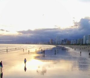 Ao olhar para a foto do pôr do sol na Praia Grande, é possível sentir uma sensação de paz e serenidade. O sol está se pondo no horizonte, tingindo o céu de tons alaranjados e vermelhos, enquanto a silhueta de palmeiras e coqueiros se destaca contra o céu. As ondas suaves do mar e a brisa fresca completam a atmosfera relaxante e envolvente do cenário. A Praia Grande é um dos destinos mais populares da região, e oferece uma variedade de opções de lazer e entretenimento para os visitantes. Durante o dia, é possível se refrescar nas águas claras da praia, praticar esportes aquáticos, ou simplesmente relaxar ao sol em uma das muitas cadeiras de praia disponíveis. À noite, a praia se transforma em um ponto de encontro para os moradores locais e turistas, com uma animada vida noturna que inclui bares, restaurantes e shows. Mas é no pôr do sol que a Praia Grande revela sua verdadeira magia. O espetáculo da natureza é uma atração imperdível, e muitos visitantes se reúnem na praia para admirar o sol se pôr no horizonte. É um momento de contemplação e reflexão, onde se pode apreciar a beleza da vida e da natureza, e sentir-se em paz consigo mesmo e com o mundo ao redor. Em resumo, a Praia Grande é um destino completo, que oferece belezas naturais, atividades de lazer, boa infraestrutura e uma atmosfera acolhedora e envolvente. A foto do pôr do sol é um lembrete daquilo que a praia tem de melhor: uma beleza natural indescritível, que se mistura com a alegria e a vitalidade de seus visitantes. Certamente, um destino que vale a pena conhecer e explorar.